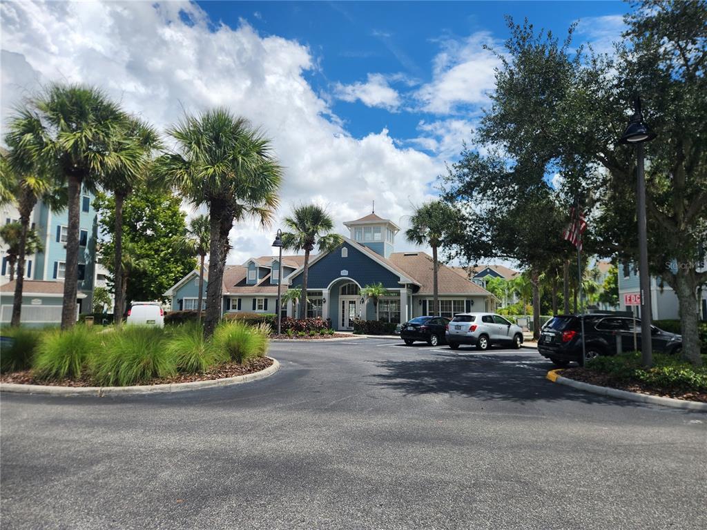 A blue community clubhouse building stands behind a parking lot with palm trees and landscaping — 5257 CANE ISLAND LOOP UNIT 302, KISSIMMEE, FL