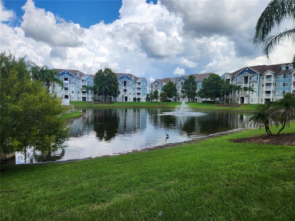 A pond with a fountain sits in front of several multi-story apartment buildings — 5257 CANE ISLAND LOOP UNIT 302, KISSIMMEE, FL
