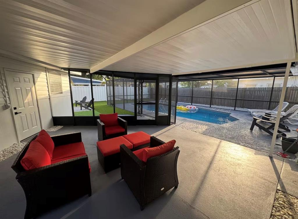 A covered patio with red cushioned furniture overlooks a screened-in swimming pool and backyard — 2446 SHELLEY STREET, CLEARWATER, FL