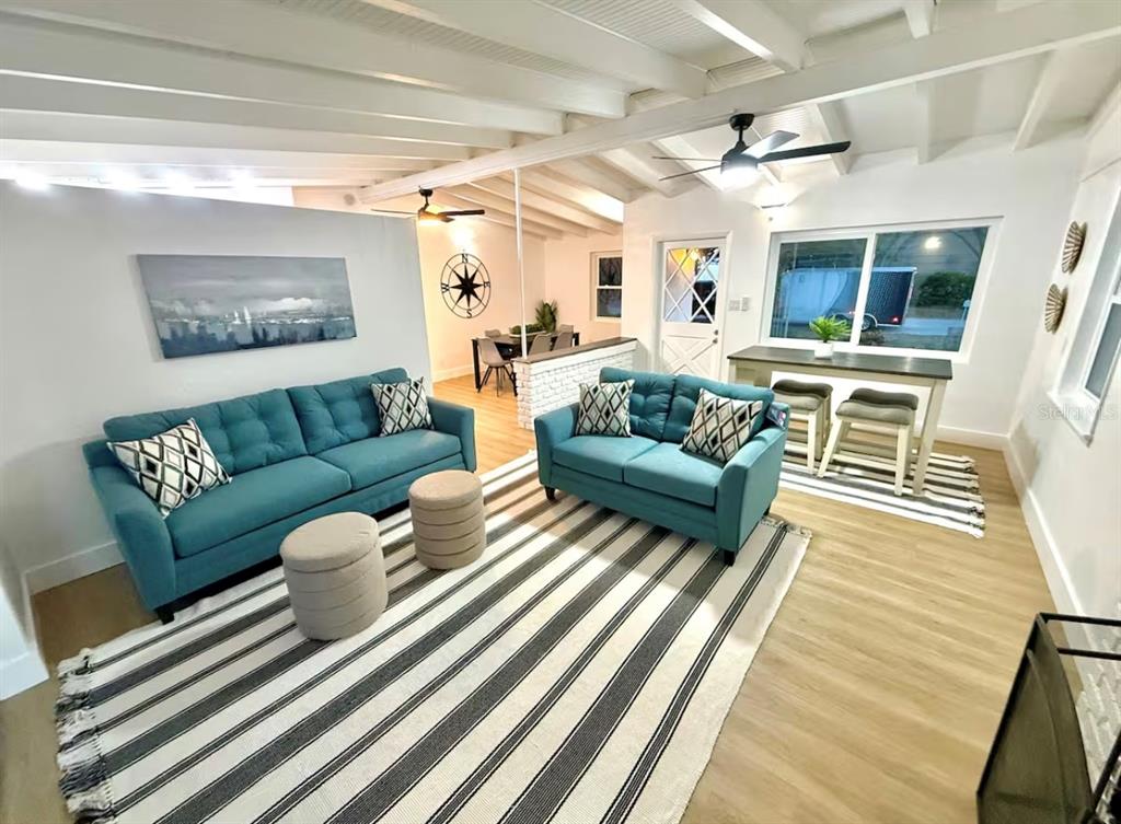 A living room features two teal sofas, a striped rug, and a dining area beyond — 2446 SHELLEY STREET, CLEARWATER, FL