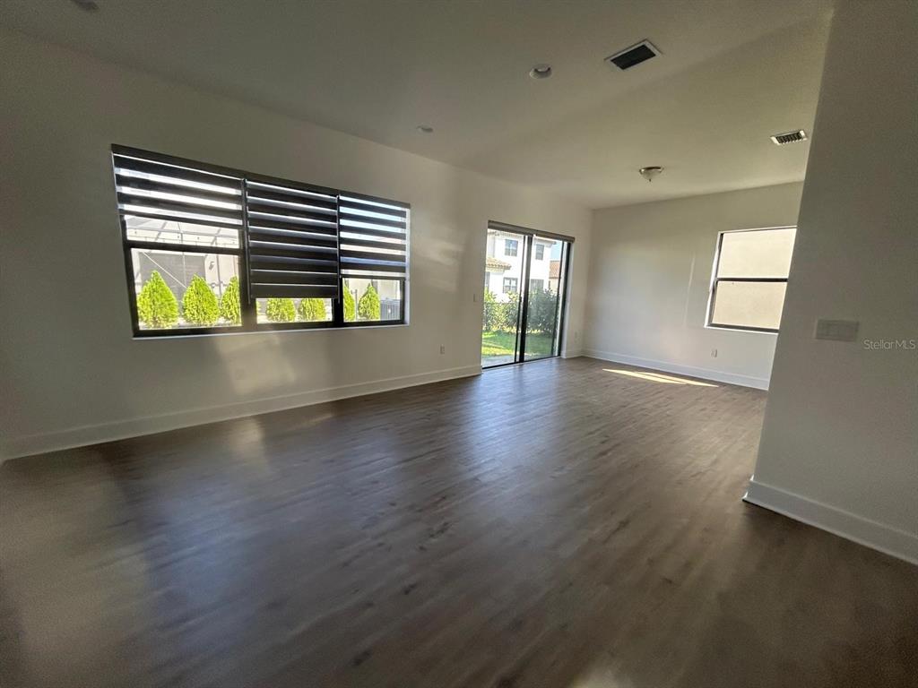 An empty living area features light wood-look flooring, white walls, large windows, and sliding doors — 5525 AGOSTINO WAY, AVE MARIA, FL
