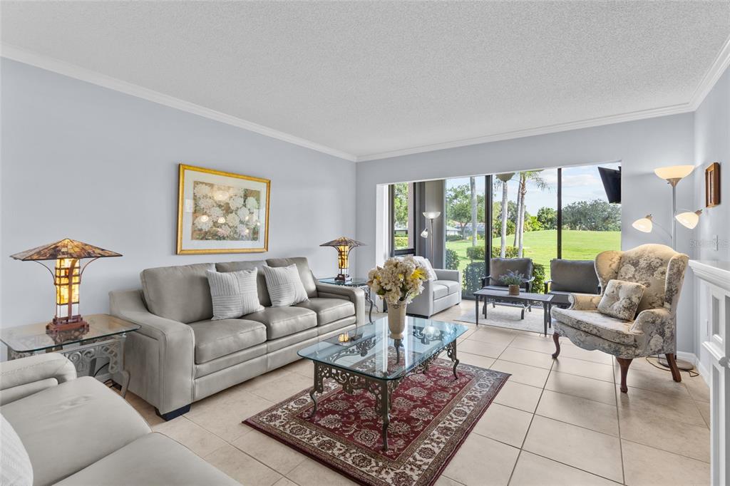 A living room features a grey sofa, patterned armchair, glass coffee table, and large sliding doors — 6211 TIMBER LAKE DRIVE UNIT B1, SARASOTA, FL