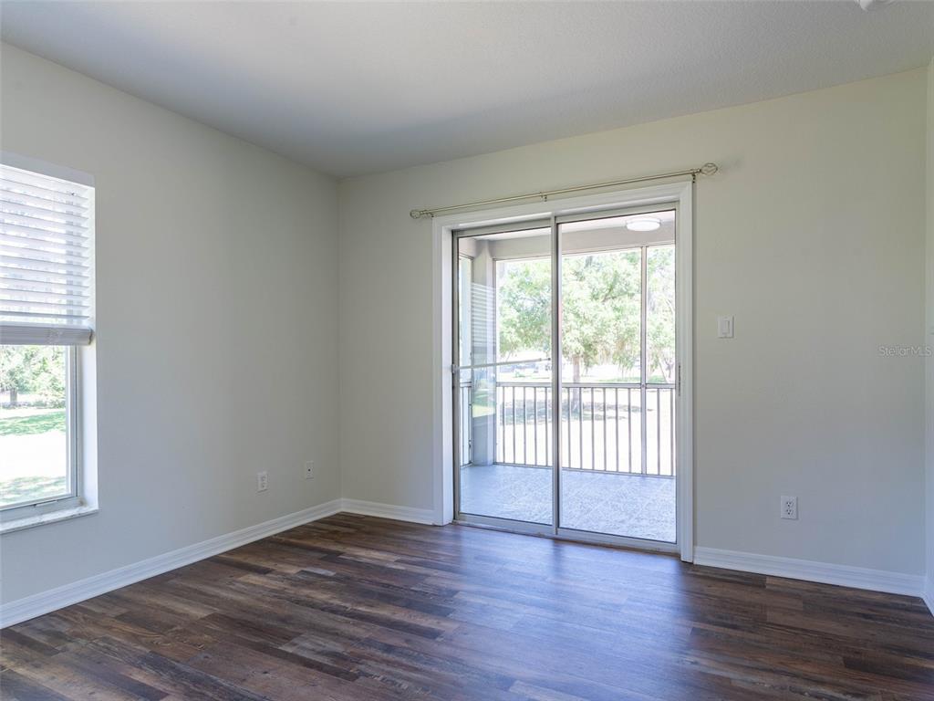 An empty room features wood-look flooring, a window, and sliding glass doors to a patio — 36921 VALUE CIRCLE, DADE CITY, FL