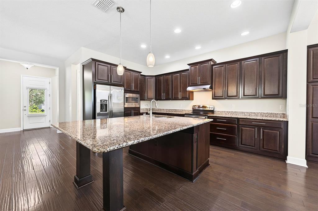 A kitchen with dark wood cabinets, granite countertops, a large island, and hardwood flooring — 8130 LAUREATE BOULEVARD, ORLANDO, FL