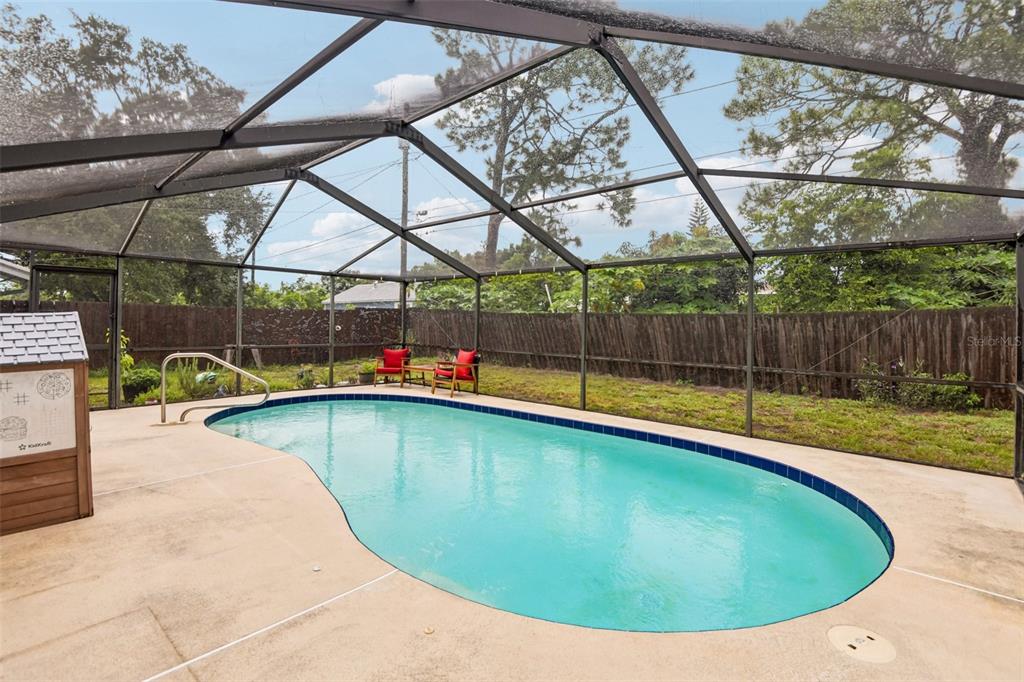 A screened-in backyard features a kidney-shaped swimming pool and a wooden fence — 8401 PORTULACA AVENUE, SEMINOLE, FL