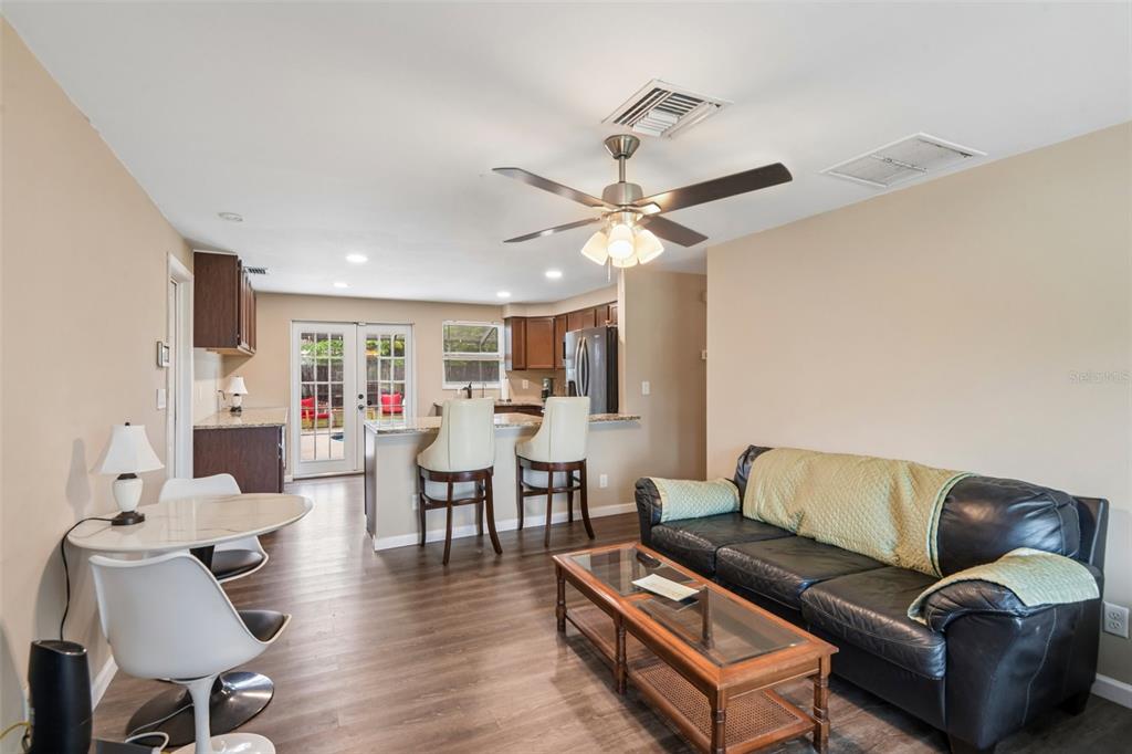 An open-concept living and dining area features wood-look flooring, a ceiling fan, and kitchen access — 8401 PORTULACA AVENUE, SEMINOLE, FL