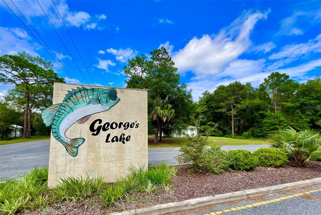 A stone monument sign featuring a painted fish and the text George's Lake stands outdoors — 1150 CORAL FARMS ROAD, FLORAHOME, FL