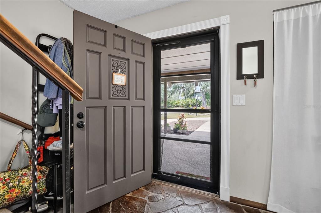 An open front door reveals a stone-floored entryway with a staircase and a screen door — 2 TIMBERLINE TRAIL UNIT B, ORMOND BEACH, FL