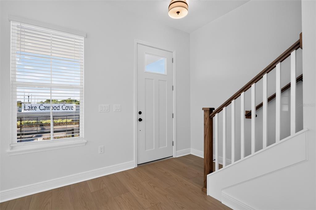 An entryway features light wood flooring, a white front door, and a staircase with railings — 13325 LUSH LIME ALLEY, WINDERMERE, FL