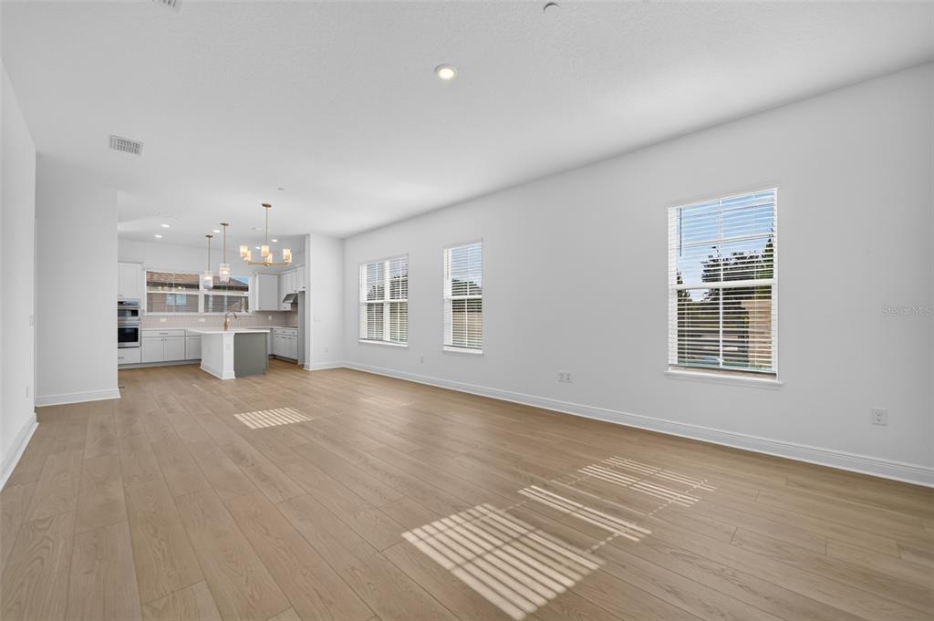 An open-concept living area with light wood flooring, white walls, and an adjacent kitchen — 13325 LUSH LIME ALLEY, WINDERMERE, FL