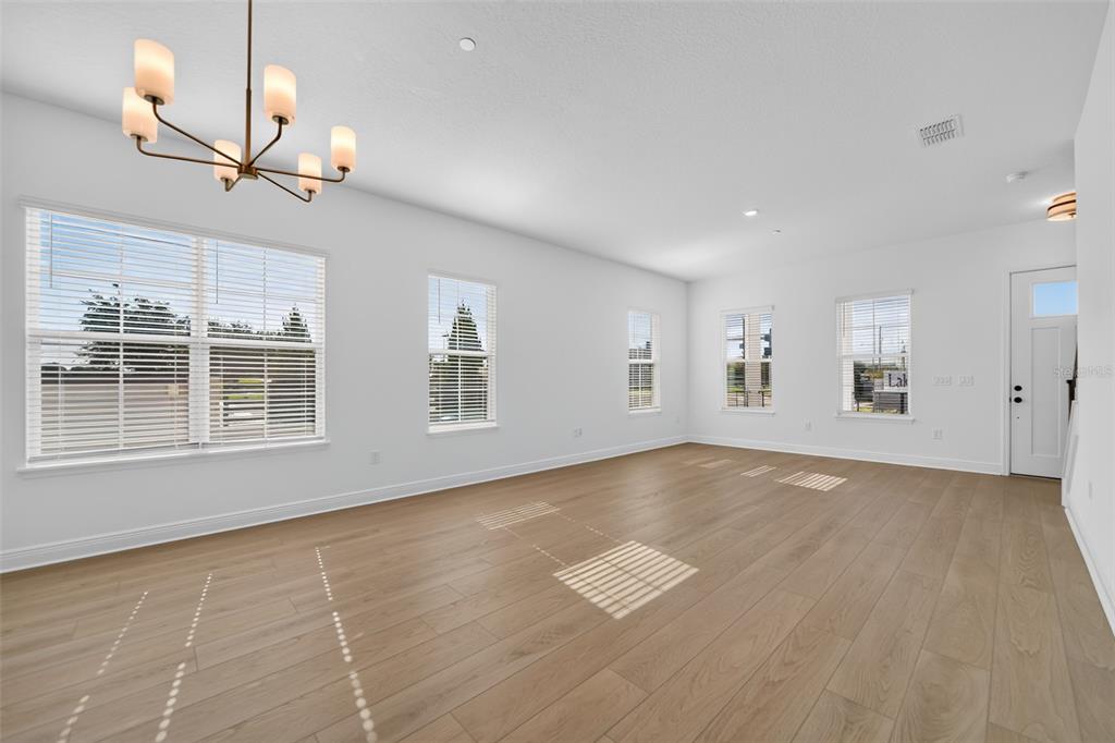 An empty room with light wood floors, white walls, a chandelier, and several windows — 13325 LUSH LIME ALLEY, WINDERMERE, FL