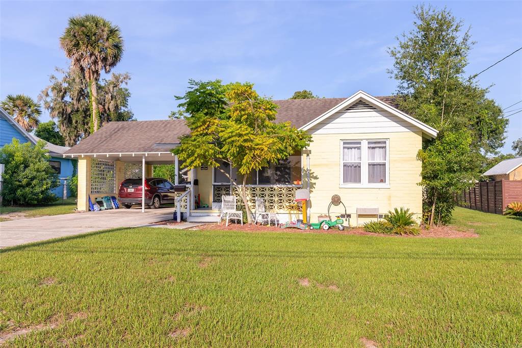 A yellow single-story house features a front carport, a covered porch, and a grassy lawn — 220 N ADELLE AVENUE, DELAND, FL
