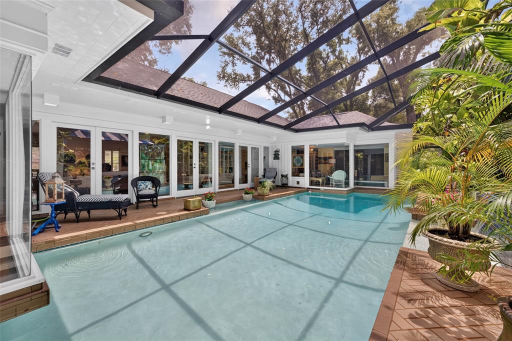 An indoor swimming pool enclosed by a screened lanai with wooden decking and glass doors — 602 S RIVERHILLS DRIVE, TEMPLE TERRACE, FL