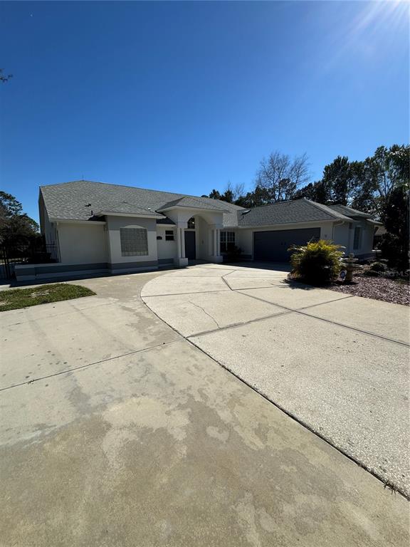 A single-story house with a light-colored stucco exterior, a gray shingled roof, and a concrete driveway — 7565 JOMEL DRIVE, WEEKI WACHEE, FL