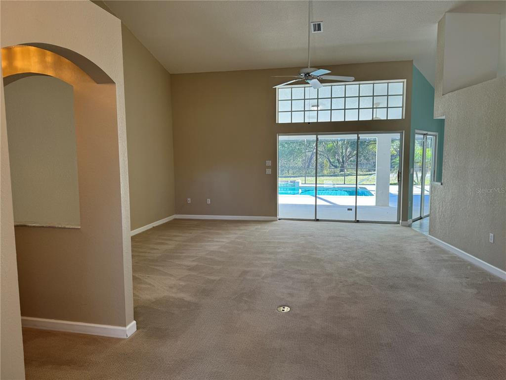 A spacious living room with beige carpet, vaulted ceilings, and sliding glass doors to a pool — 7565 JOMEL DRIVE, WEEKI WACHEE, FL