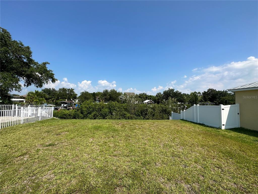 A grassy backyard features a white vinyl fence and views of trees and water — 421 BAHAMA GRANDE BOULEVARD, APOLLO BEACH, FL