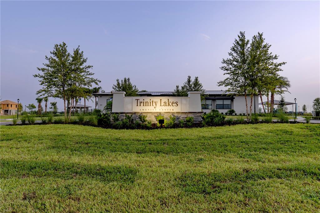 A stone monument sign for Trinity Lakes Amenity Center stands before a modern community building — 7272 ROLLING LEAF ROAD, GROVELAND, FL