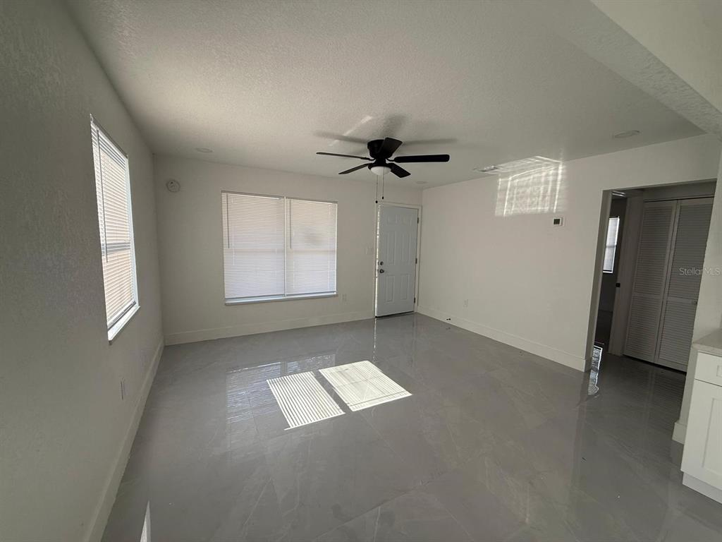 A bright, empty living room features white walls, a ceiling fan, and light-colored tile flooring — 427 40TH AVENUE S, ST PETERSBURG, FL