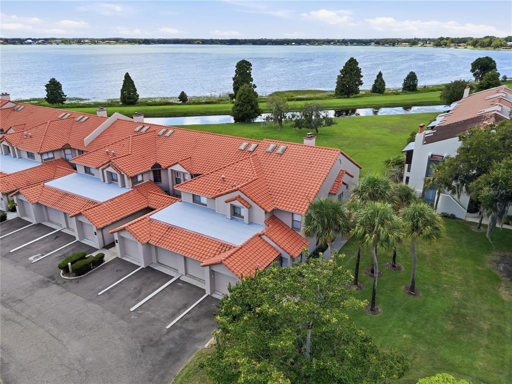 An aerial view shows a multi-unit townhouse complex with red tile roofs near a lake — 701 MAGNOLIA PLACE, WINTER HAVEN, FL