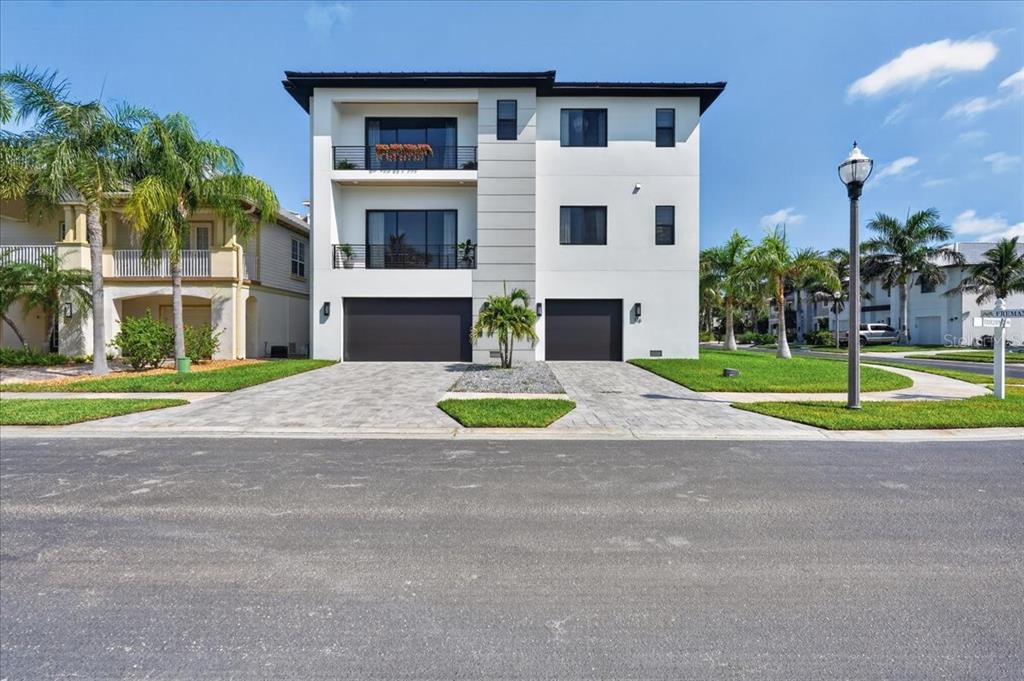 A modern three-story white house with two garages and two balconies stands on a street — 116 WIMBLEDON COURT, REDINGTON SHORES, FL