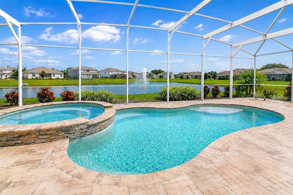 A swimming pool and spa with stone tiling inside a screened-in lanai overlooking a pond — 8871 BACKSPIN LANE, DAVENPORT, FL