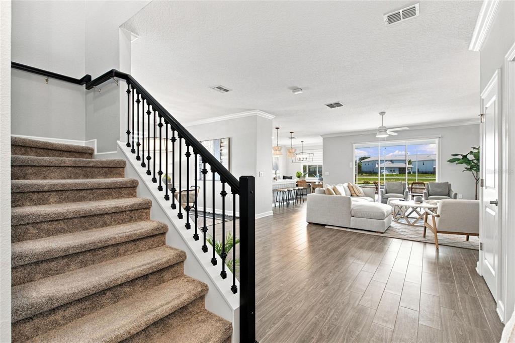 A carpeted staircase with a black railing leads to an open-concept living area and kitchen — 8871 BACKSPIN LANE, DAVENPORT, FL