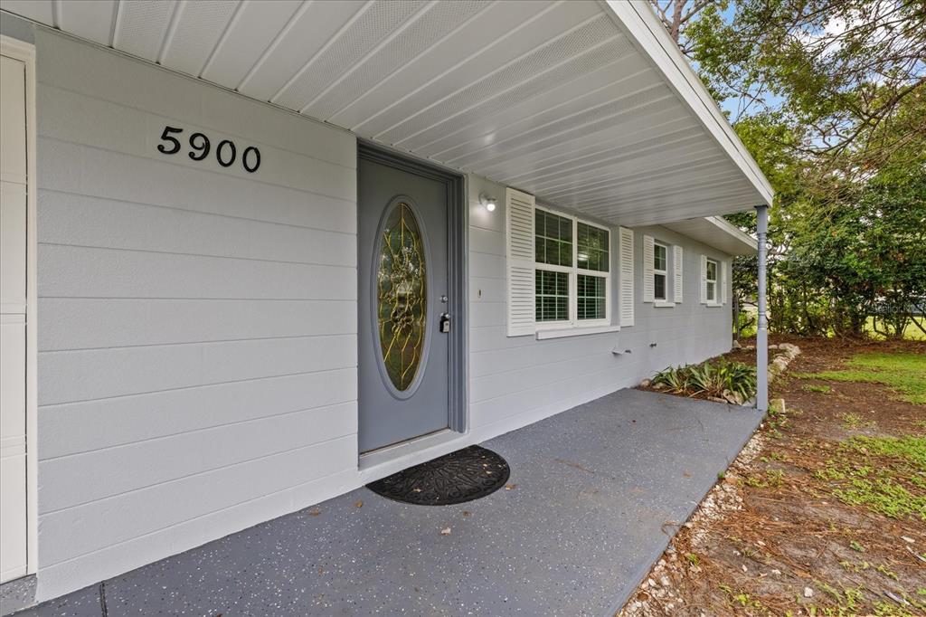 A gray house exterior features a front porch, a glass-paneled door, and white window shutters — 5900 AVOCADO STREET, ZEPHYRHILLS, FL