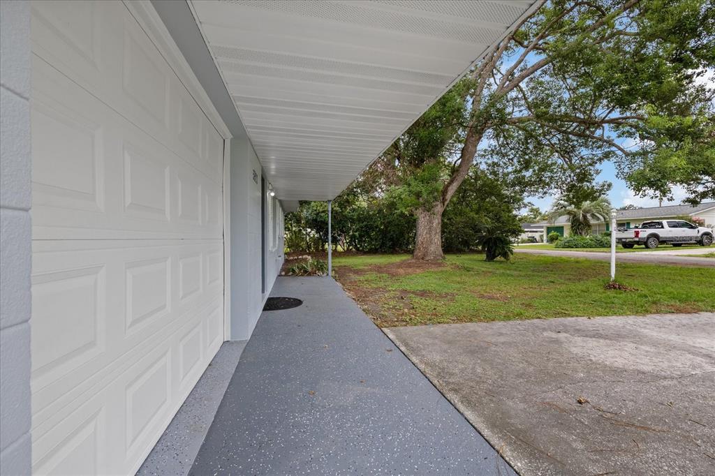 A gray painted concrete walkway leads along the side of a house with a garage — 5900 AVOCADO STREET, ZEPHYRHILLS, FL