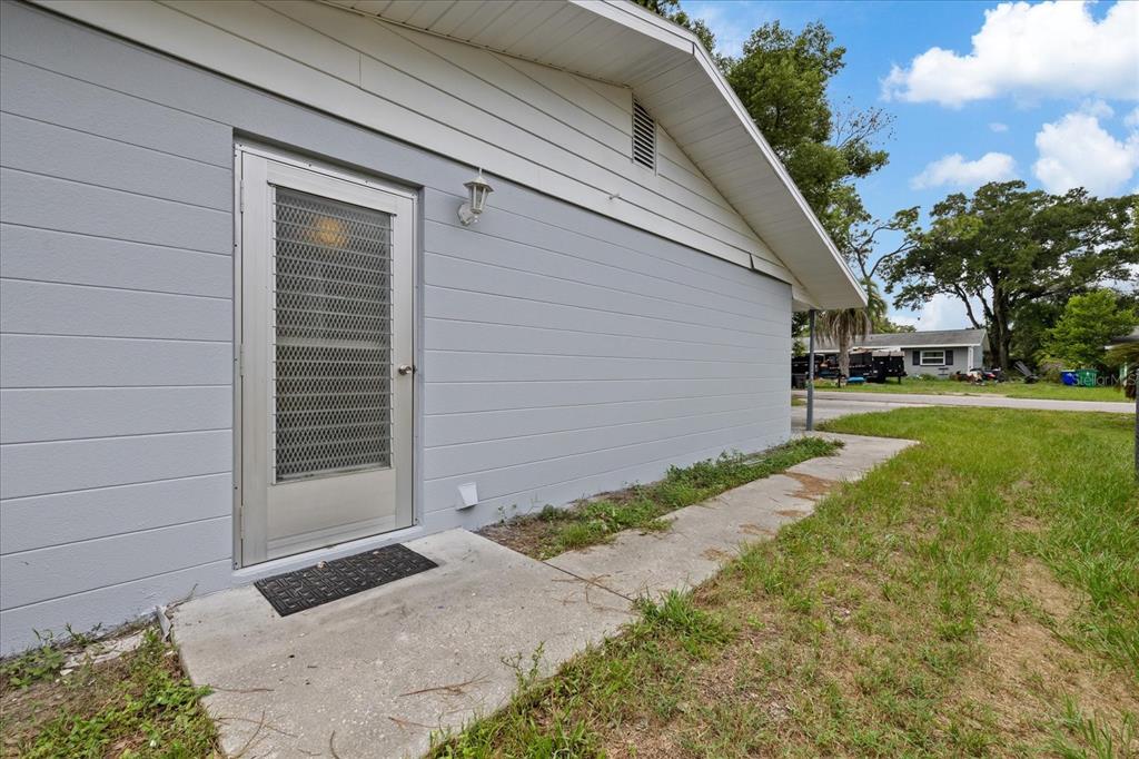 A gray exterior wall features a metal screen door and a concrete walkway — 5900 AVOCADO STREET, ZEPHYRHILLS, FL