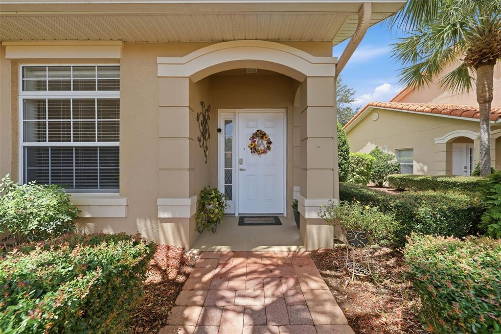 A front entrance with a white door, a brick walkway, and landscaping under a portico — 5418 COMPASS POINT, OXFORD, FL