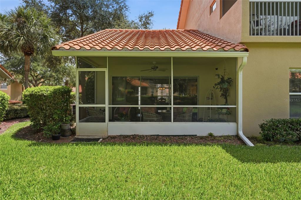 A screened-in patio with a tiled roof sits adjacent to a tan stucco house — 5418 COMPASS POINT, OXFORD, FL