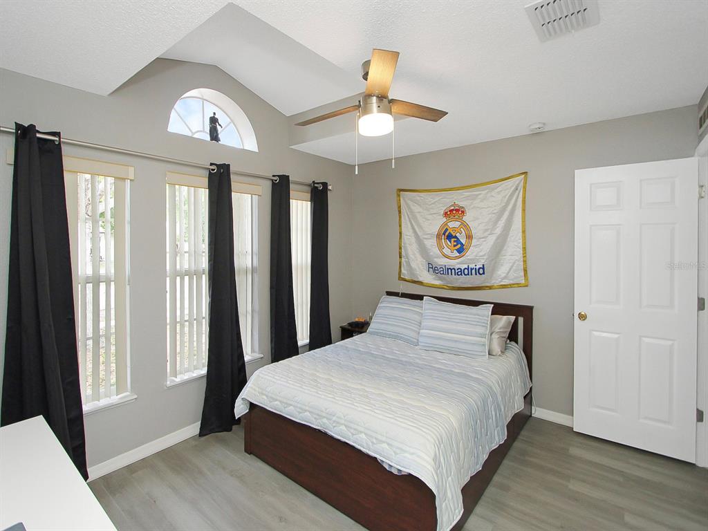 A bedroom features a bed with a Real Madrid flag, gray flooring, and vaulted ceilings — 2927 ELBIB DR, ST CLOUD, FL