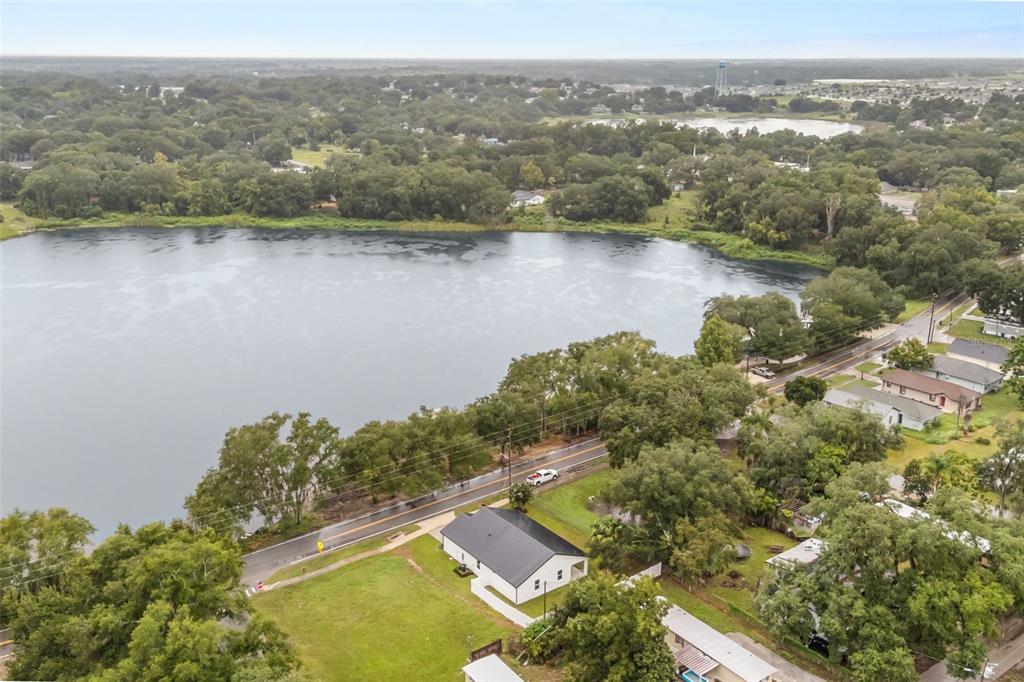 An aerial view shows a white house with a dark roof situated beside a lake — 221 S SUNSET AVENUE, MASCOTTE, FL