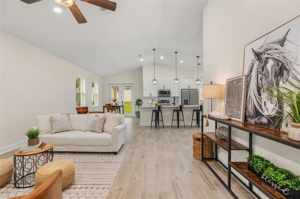An open-concept living room and kitchen featuring light wood floors, white cabinetry, and a sofa — 221 S SUNSET AVENUE, MASCOTTE, FL