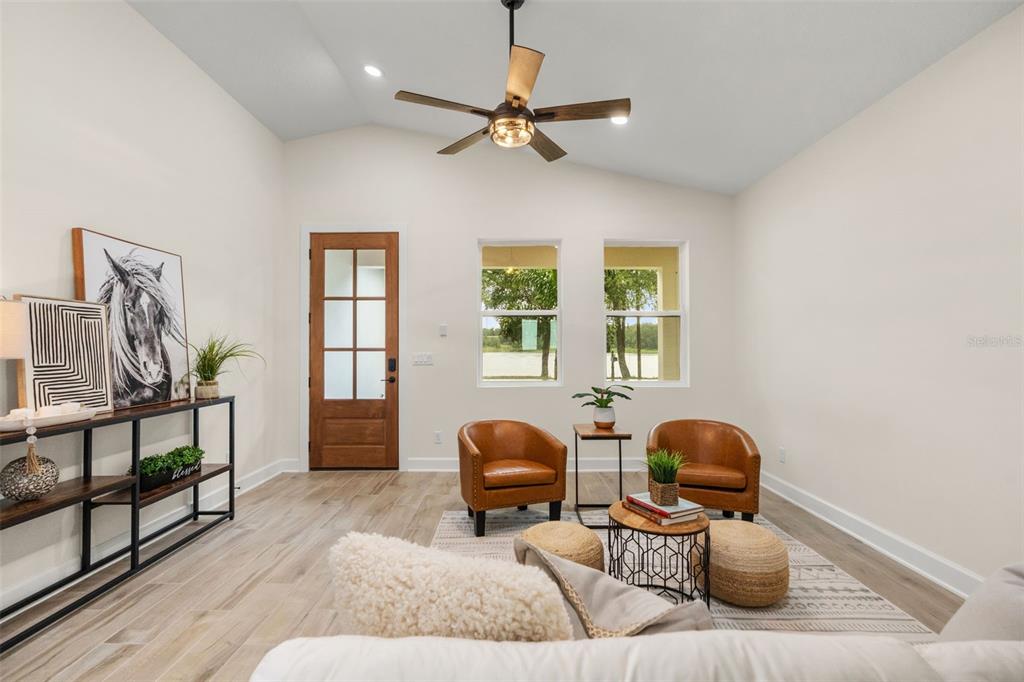 A living room features a vaulted ceiling, wood-look tile flooring, two leather chairs, and a door — 221 S SUNSET AVENUE, MASCOTTE, FL