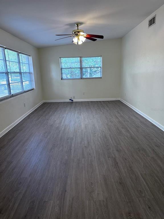 An empty room features gray wood-look flooring, a ceiling fan, and two windows — 3412 ORANOLE ROAD, ORLANDO, FL