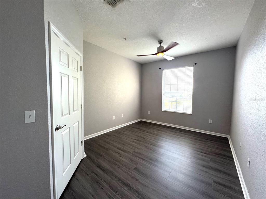 An empty bedroom features gray walls, dark wood-look flooring, a ceiling fan, and two doors — 8660 BUCCILLI DRIVE UNIT 305, ORLANDO, FL