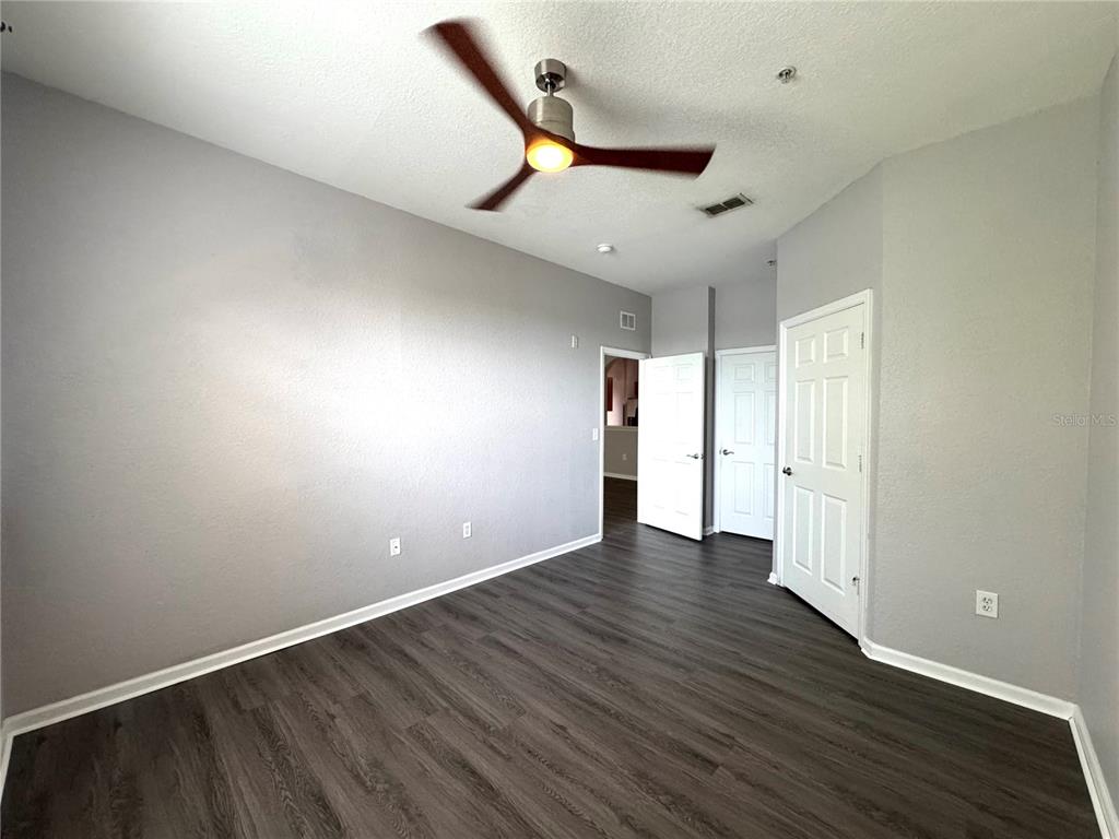 An empty living room features gray walls, wood-look flooring, a ceiling fan, and an arched pass-through — 8660 BUCCILLI DRIVE UNIT 305, ORLANDO, FL