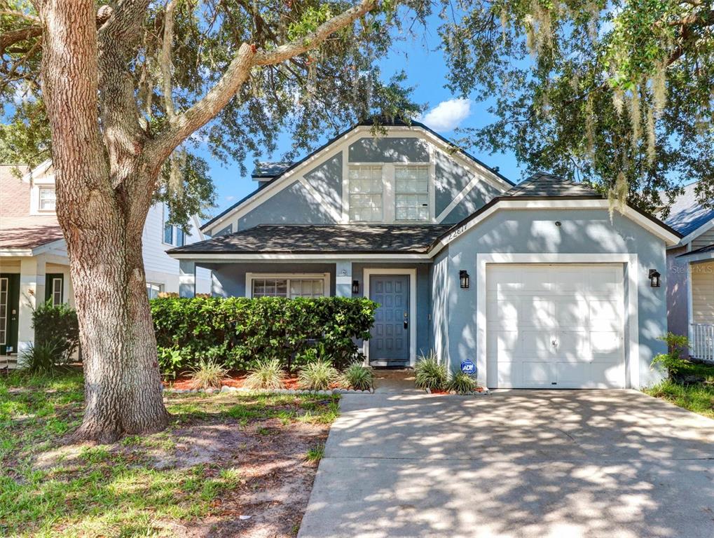 A blue two-story house features a front-facing garage, a hedge, and a large oak tree — 22817 SAINT THOMAS CIRCLE, LUTZ, FL