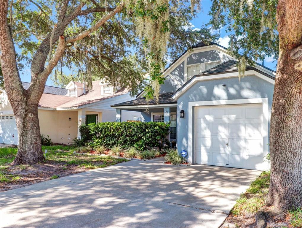 A blue house with a white garage door and a driveway sits under large trees — 22817 SAINT THOMAS CIRCLE, LUTZ, FL