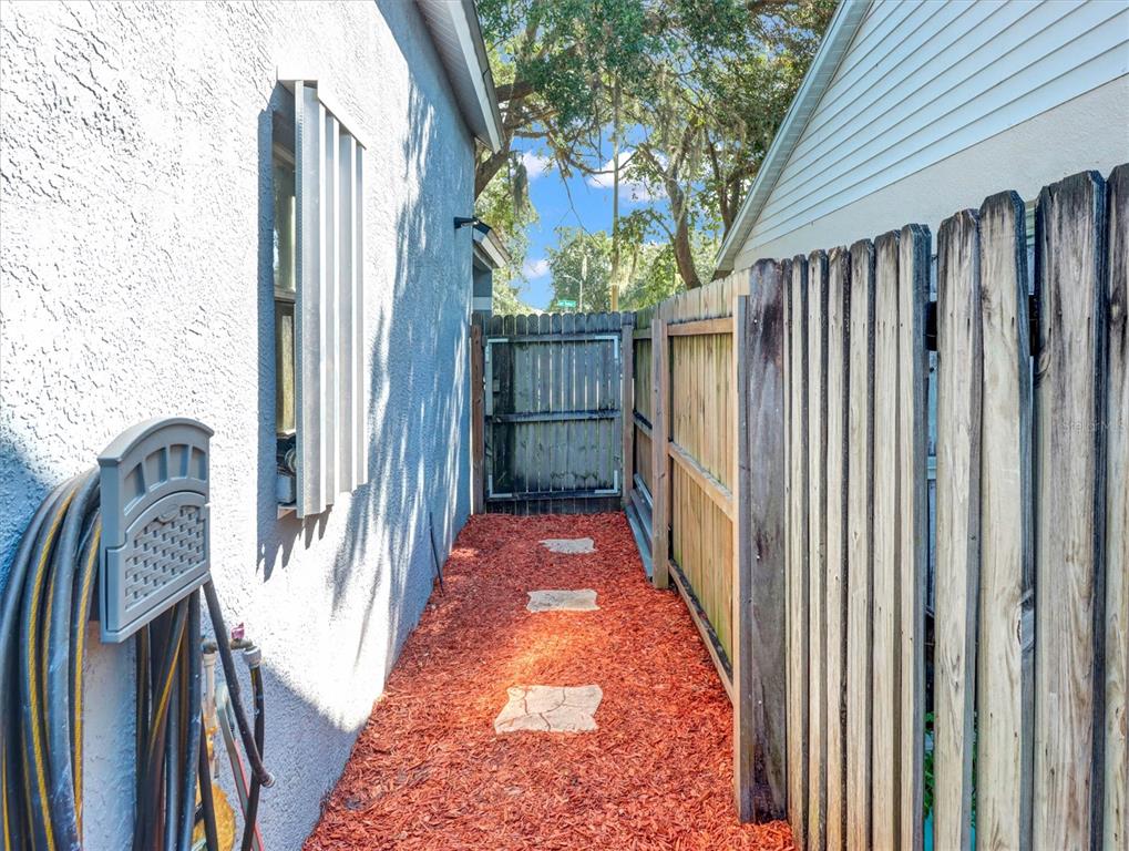 A narrow side yard features red mulch, stone pavers, and a wooden privacy fence — 22817 SAINT THOMAS CIRCLE, LUTZ, FL