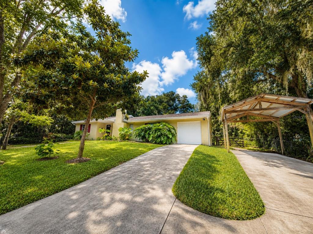 A yellow single-story house with a white garage, concrete driveway, and a wooden carport — 410 RUBY AVENUE, DELAND, FL