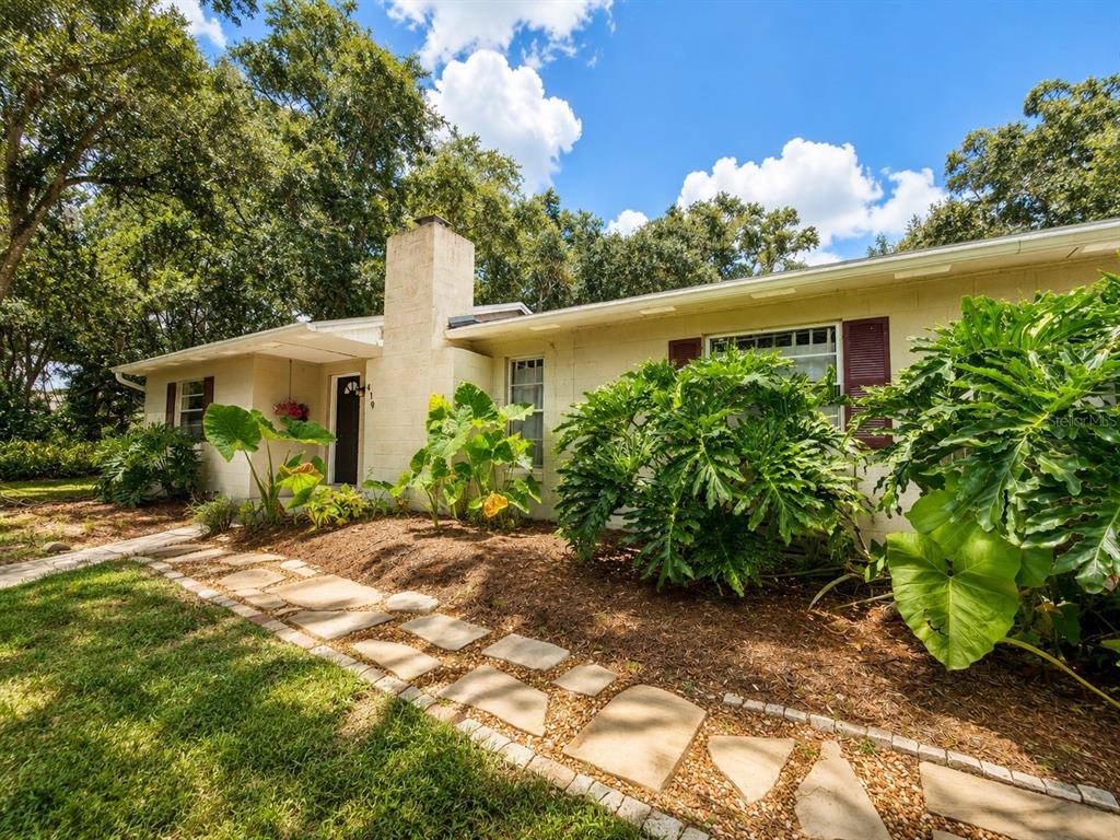 A single-story house with a stone walkway, a brick chimney, and large tropical plants — 410 RUBY AVENUE, DELAND, FL