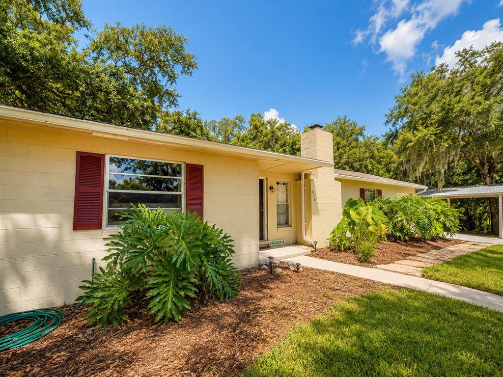 A single-story yellow house with red shutters and a stone walkway under a blue sky — 410 RUBY AVENUE, DELAND, FL