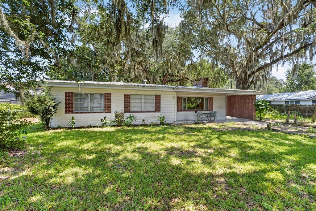 A single-story house with white siding, brick accents, and a carport under large oak trees — 12345 SE 135TH COURT, OCKLAWAHA, FL