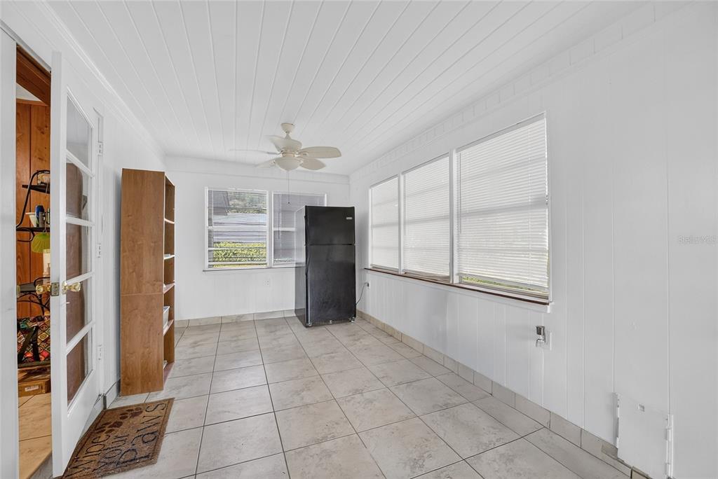 A sunroom with white paneled walls, tile flooring, a ceiling fan, and a black refrigerator — 12345 SE 135TH COURT, OCKLAWAHA, FL