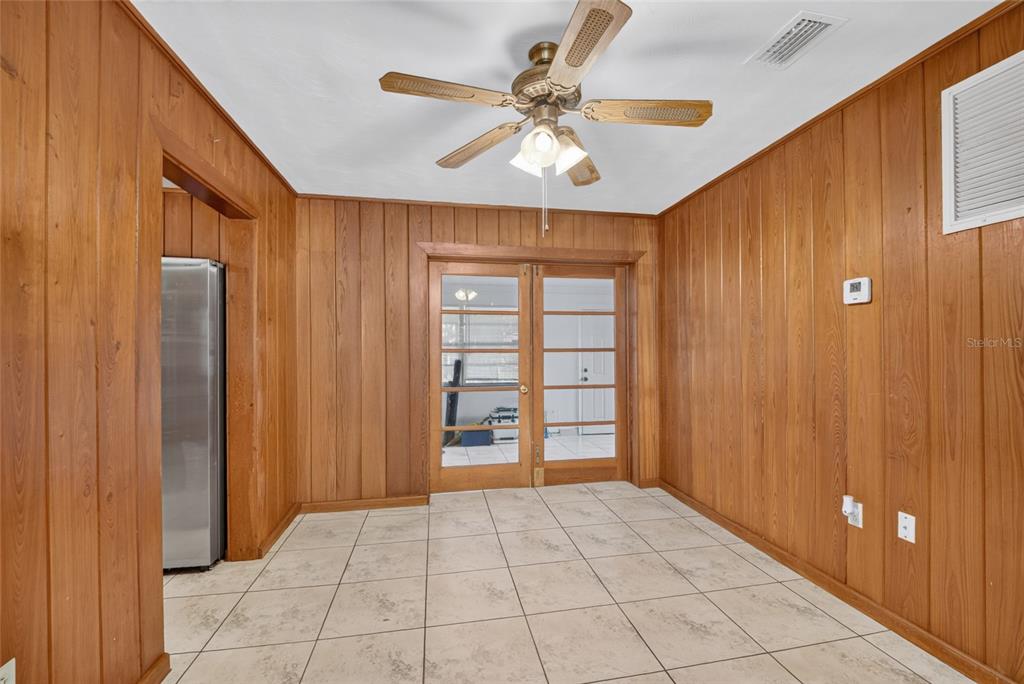 A room with wood-paneled walls, tile flooring, a ceiling fan, and glass-paned double doors — 12345 SE 135TH COURT, OCKLAWAHA, FL
