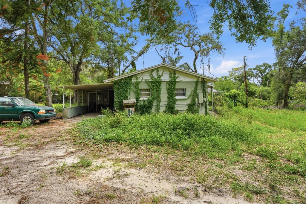 An overgrown, single-story house with a carport and ivy-covered siding sits on a dirt lot — 832 S PARSONS AVENUE, BRANDON, FL