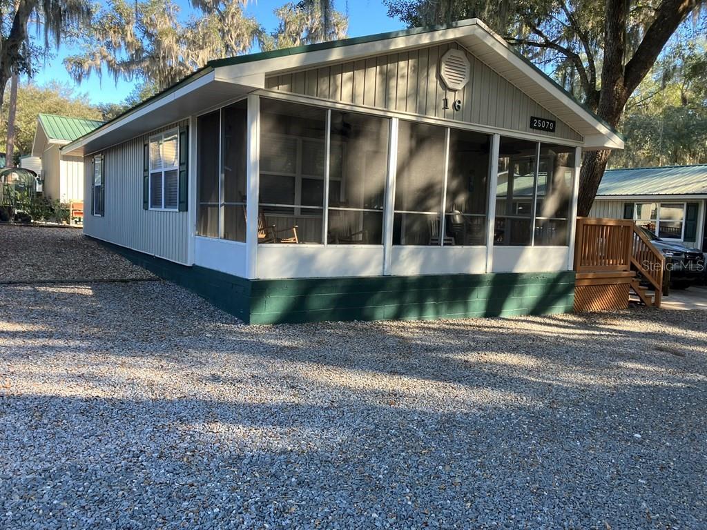 A light-colored mobile home features a large screened-in front porch and a gravel driveway — 25079 NE 140TH LOOP, SALT SPRINGS, FL