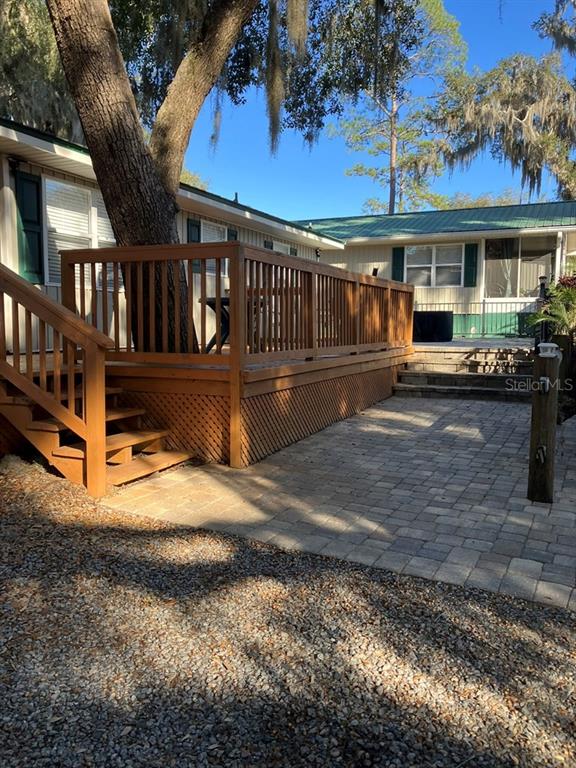 A wooden deck with a built-in tree and stone pavers sits beside a mobile home — 25079 NE 140TH LOOP, SALT SPRINGS, FL